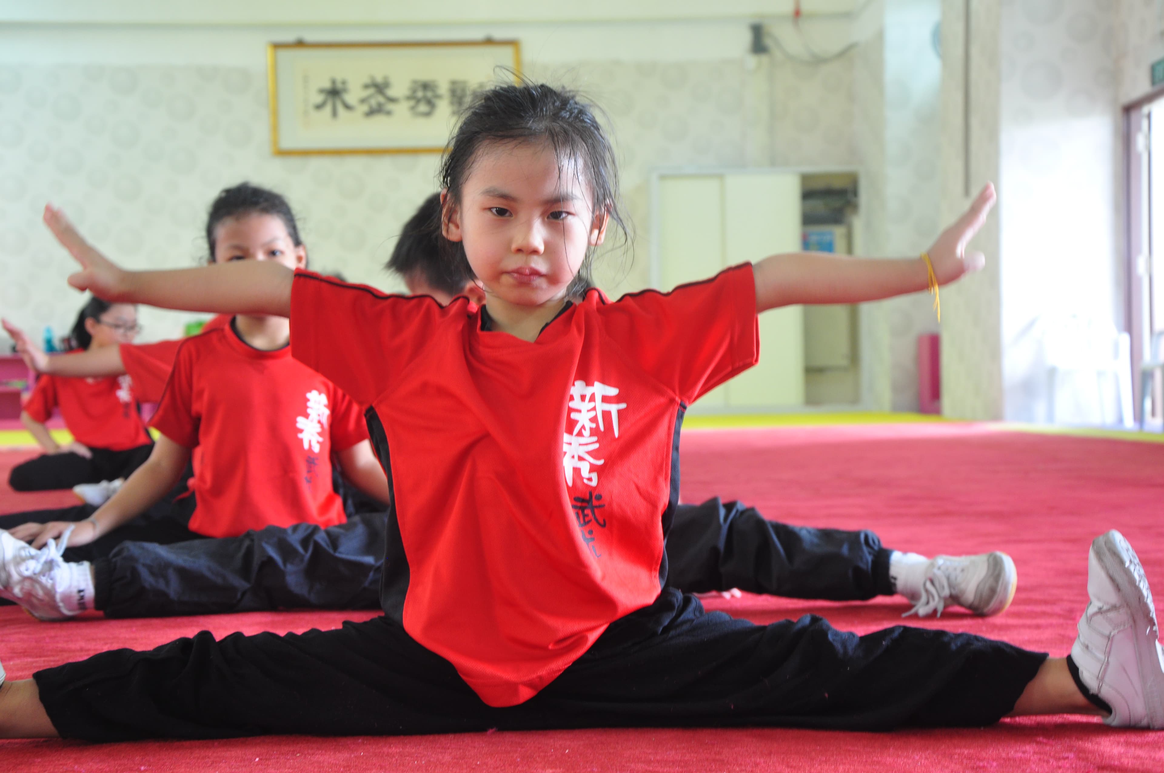 Sino Wushu students in red uniforms holding a full split with determination